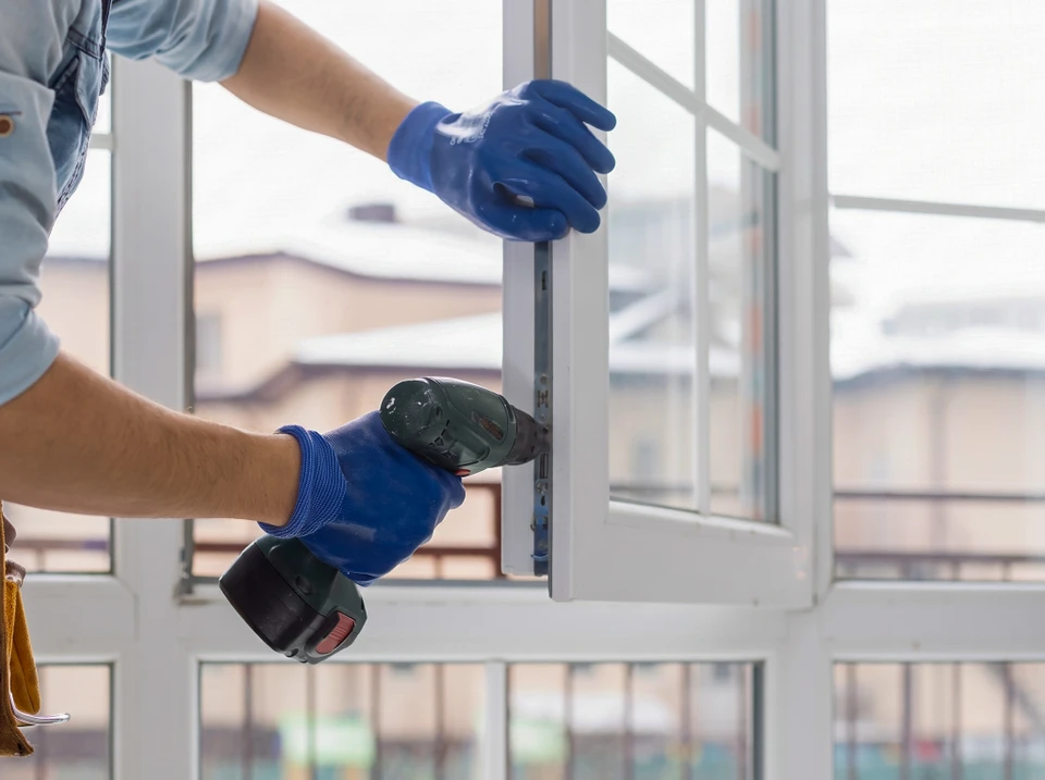 Artisan menuisier d'âge moyen, vêtu d'une tenue de travail professionnelle, tenant un document devis dans ses mains, discutant face à face avec un client propriétaire devant une fenêtre extérieure d'habitation nécessitant de l'entretien. L'artisan pointe le document en expliquant les tarifs de la prestation de maintenance.